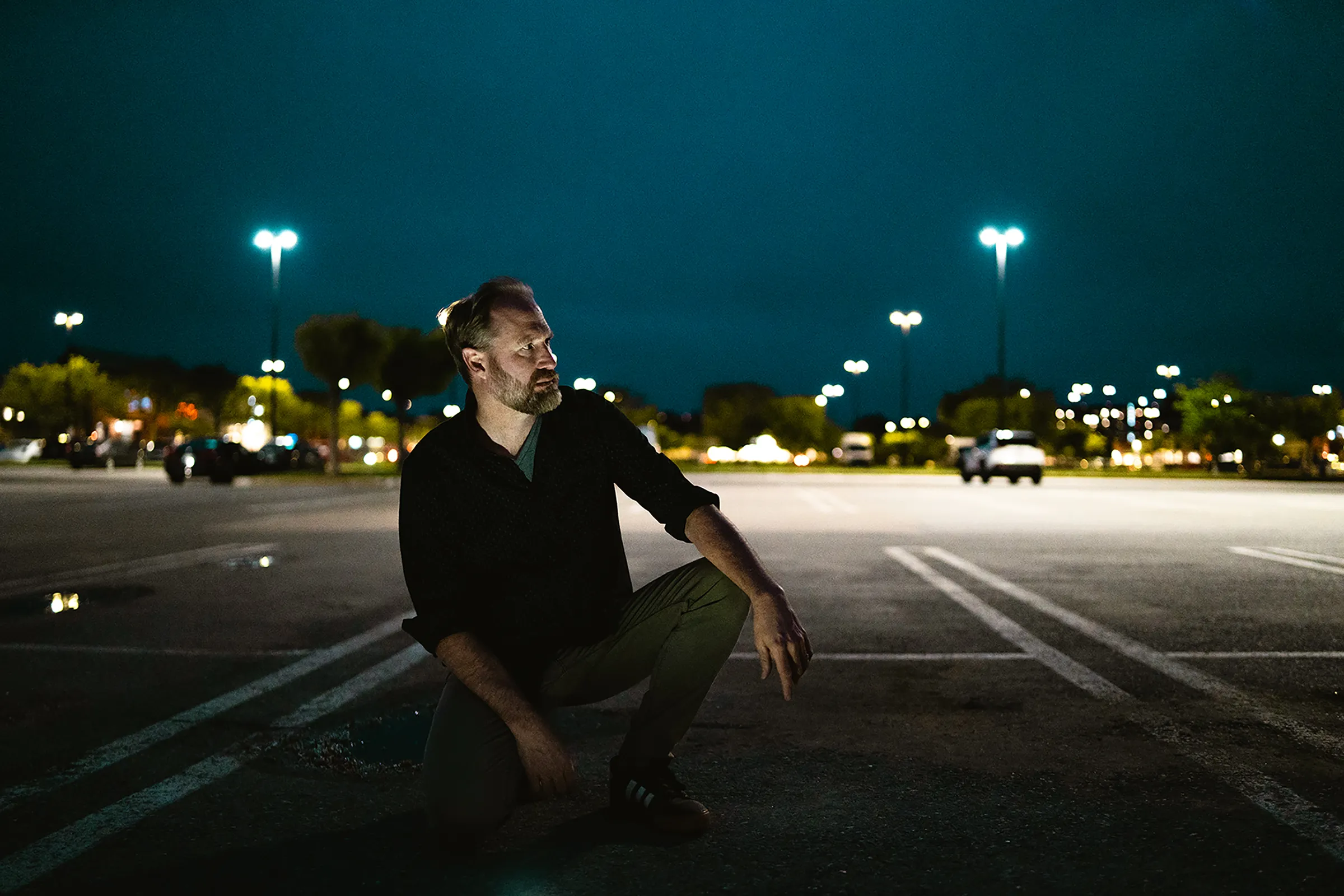 A figure crouching in a moodily lit parking lot
